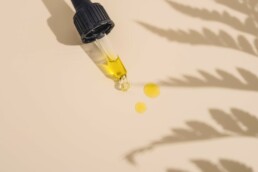 CBD oil dropper on a table with the shadow of a hemp plant over the table.